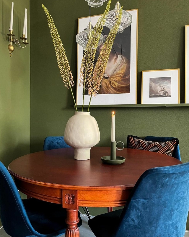 Een kleurrijke eethoek met blauwe stoelen, een houten tafel en groene muren