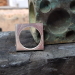 Houtskoolblokje met daarop een zilveren vierkant plaatje met een rond gat eruit gezaagd  voor de basis van een verlovingsring in de vorm van een moer