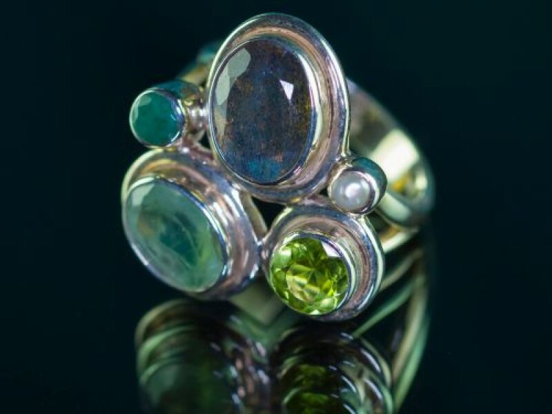 ZIlveren ring met verschillende edelstenen in blauw en groen tinten op een zwarte achtergrond