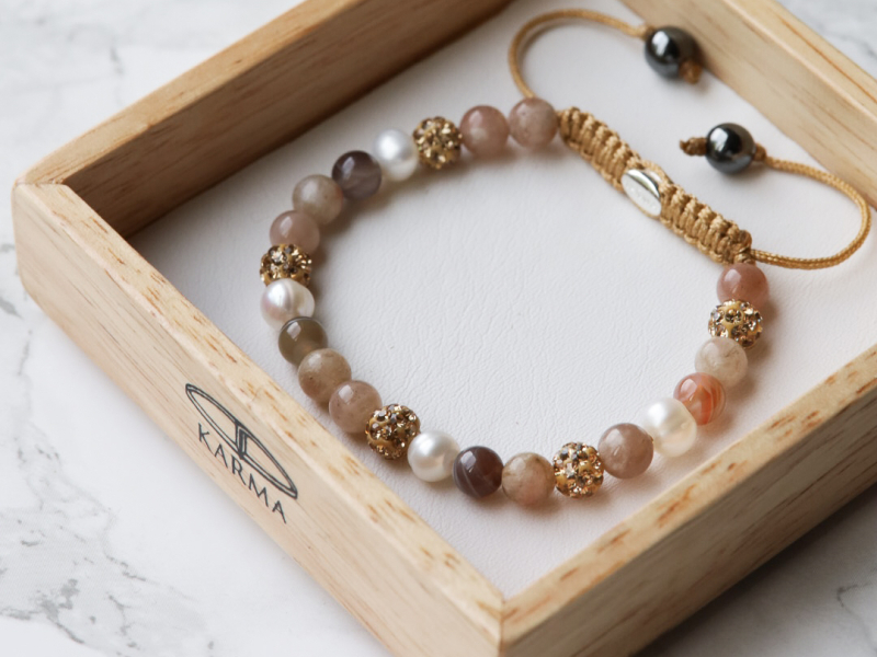Karma Jewelry armband in display van hout met een witte ondergrond en de armband is zalm, goud van kleur