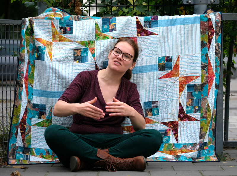 Rianne in front of butterly scrap quilt talking