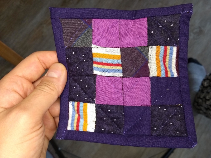 Finished coaster nine patch quilt with border made with several different purple fabrics