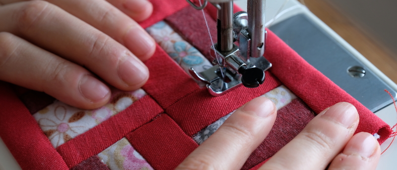Handen die een rode roman square quilt maken met een naaimachine