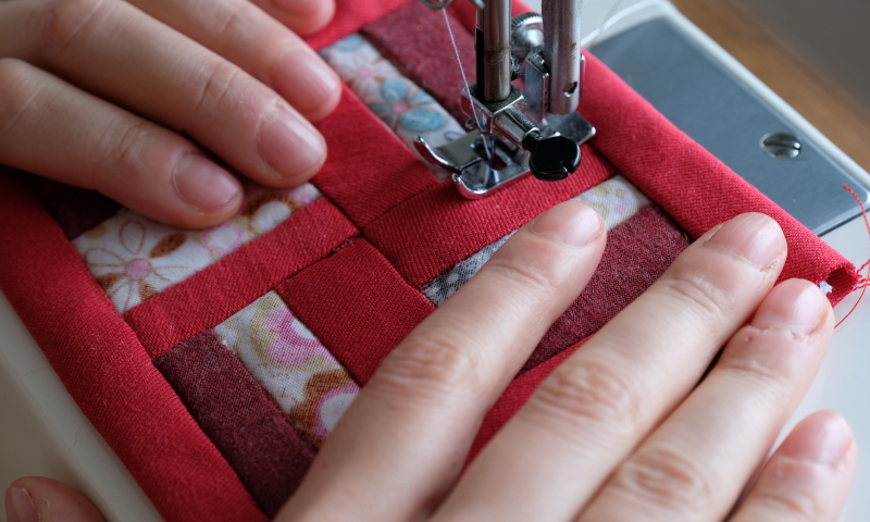 Handen die een rode roman square quilt maken met een naaimachine