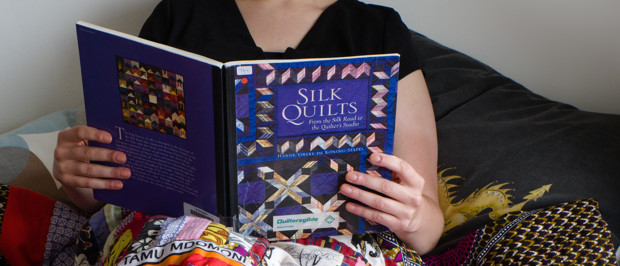 Rianne of Kick-Ass Quilts reading a book about silk quilts under a blanket