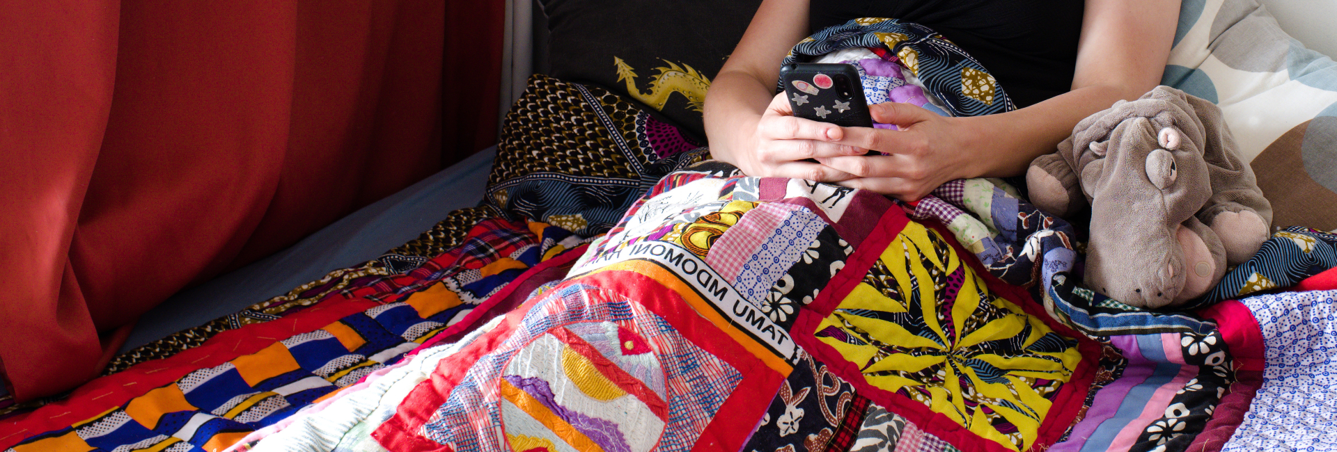 Rianne under a quilt using a phone Rianne of Kick-Ass Quilts laying under her Kenyan quilt relaxing with her phone.