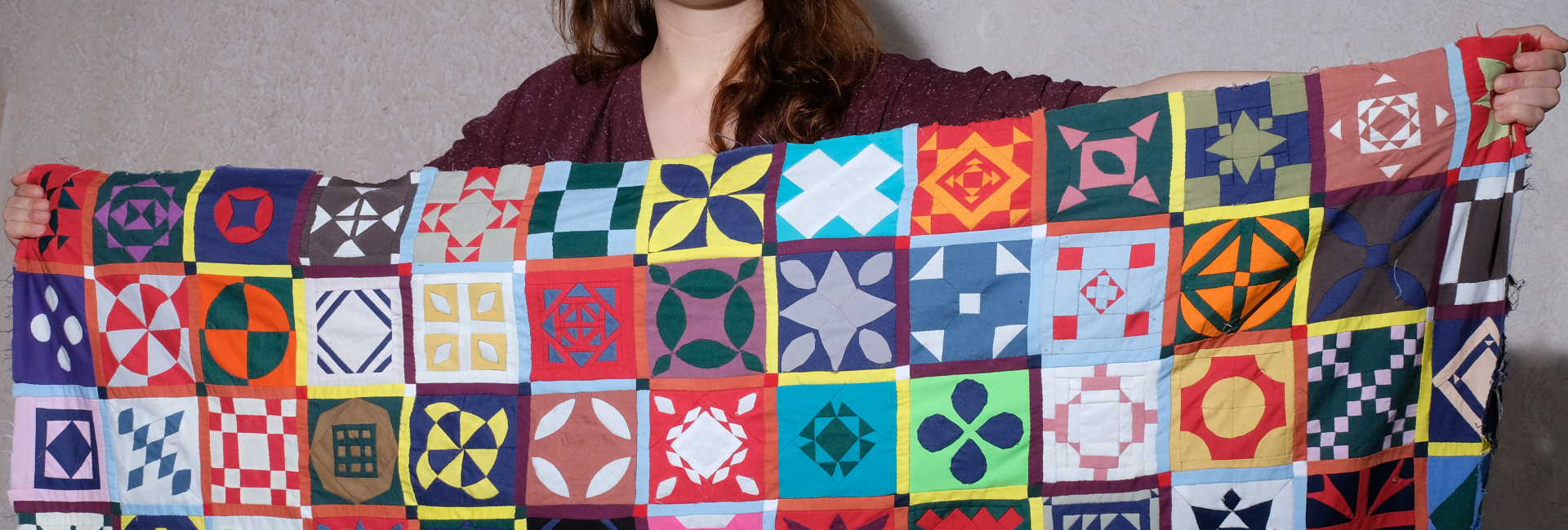 Rianne of Kick Ass Quilts holding Dear Jane Quilt Sampler made from all the colours in solid fabrics looking determined