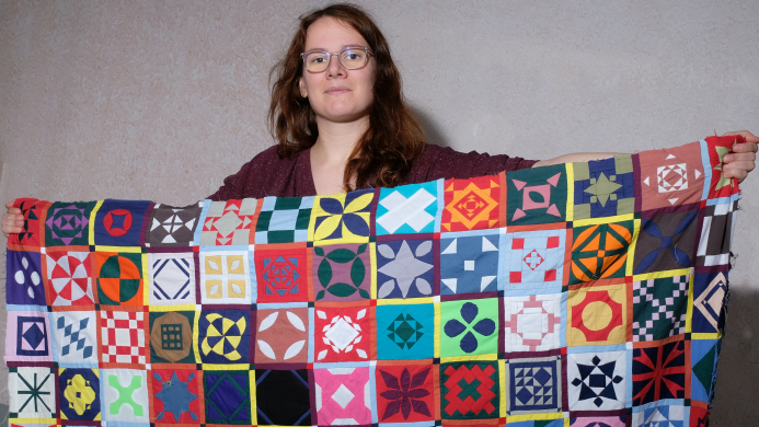 Rianne of Kick Ass Quilts holding Dear Jane Quilt Sampler made from all the colours in solid fabrics looking determined