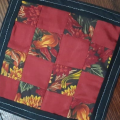 Rita Bailey mini-quilt coaster  made in a nine patch pattern with a combination of red solid fabrics and fabric with autumn leaves