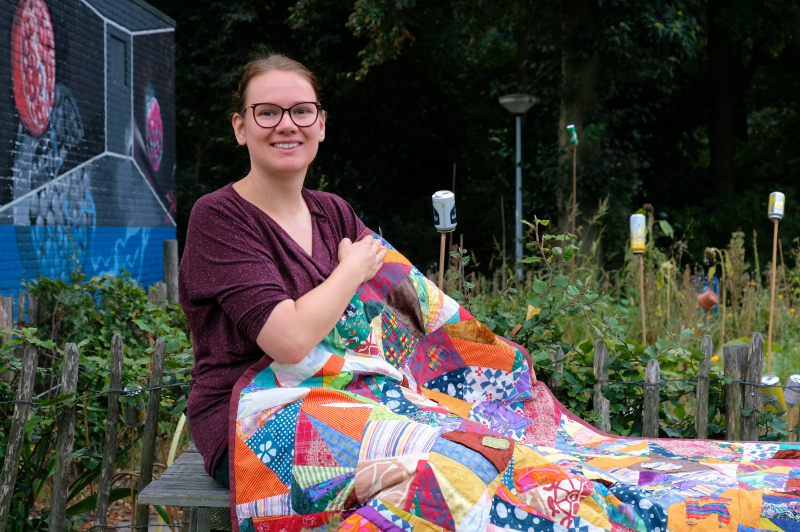 Rianne with her  crazy quilt Picknick quilt sitting dow with flowers and graffiti in the background
