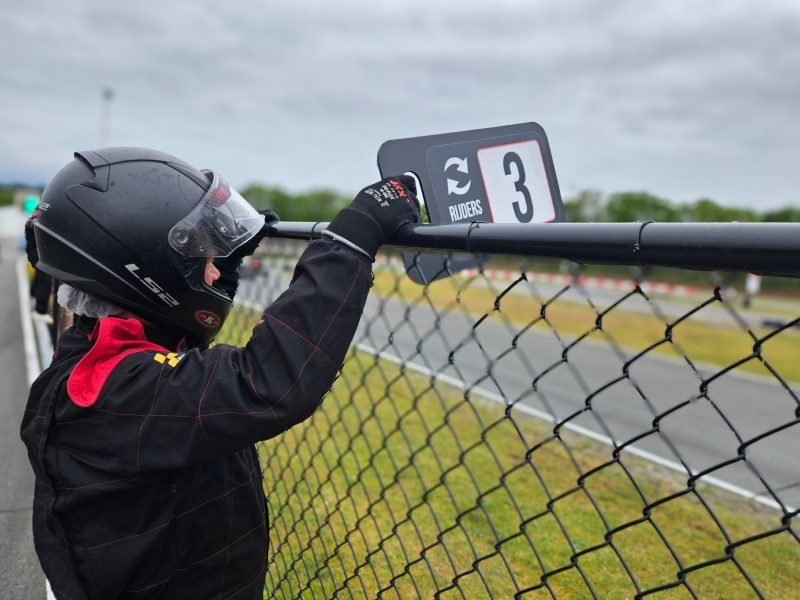 Deelnemer houdt rijderswissel bord 3 bij hek Circuit Park Berghem