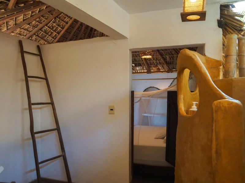 Houten ladder en open badkamer met handgemaakt houten element in een cabin van Un Sueño, met doorkijkje naar de slaapkamer onder rietdak