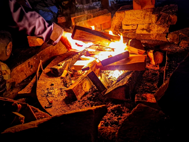 Hand legt hout op het vuur in een vuurplaats tijdens de cabin-break bij de sneeuwscooter safari in Tahko