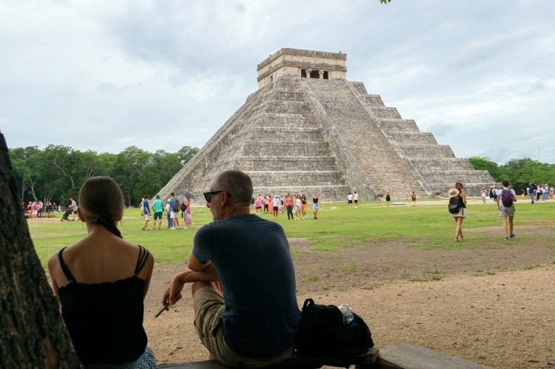 Rustmoment met uitzicht op El Castillo Twee bezoekers die in de schaduw zitten met uitzicht op El Castillo in Chichén Itzá.
