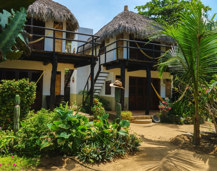 Twee rietgedekte familiecabins van Un Sueño omgeven door weelderige tropische tuin met cactussen, palmen en bloemen in San Agustinillo Mexico