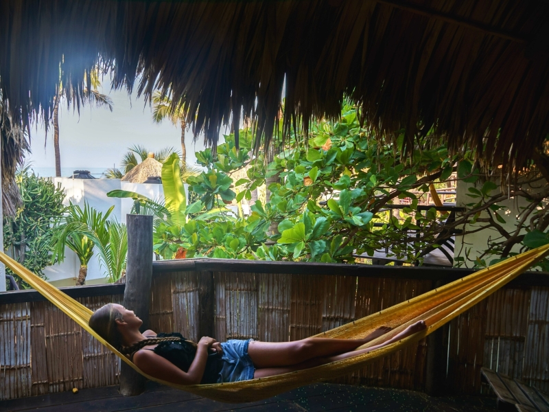 Uitzicht vanuit het overdekte terras van een cabin bij Un Sueño, met hangmat en doorkijkje naar de Stille Oceaan door palmbladeren en rietdak