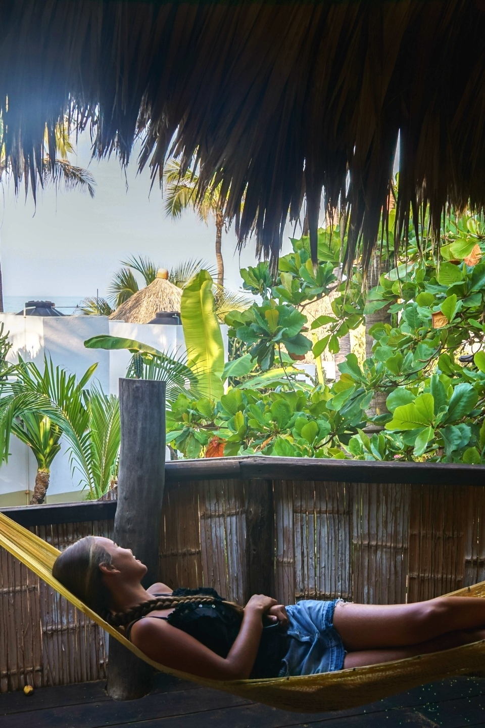 Uitzicht vanuit het overdekte terras van een cabin bij Un Sueño, met hangmat en doorkijkje naar de Stille Oceaan door palmbladeren en rietdak