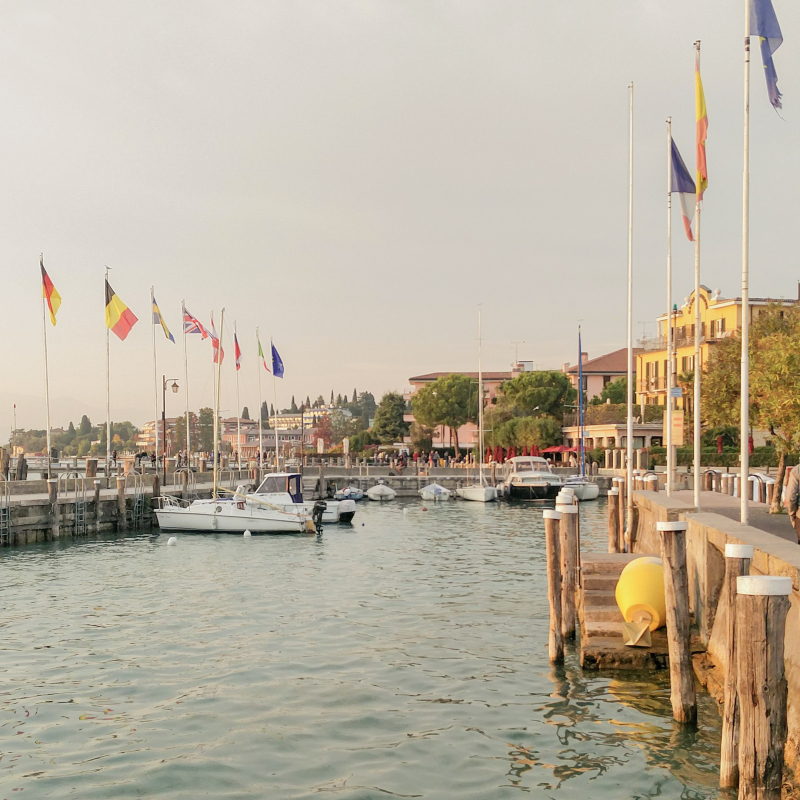 Haven aan het Gardameer met bootjes en vlaggen bij Sirmione in de avondzon