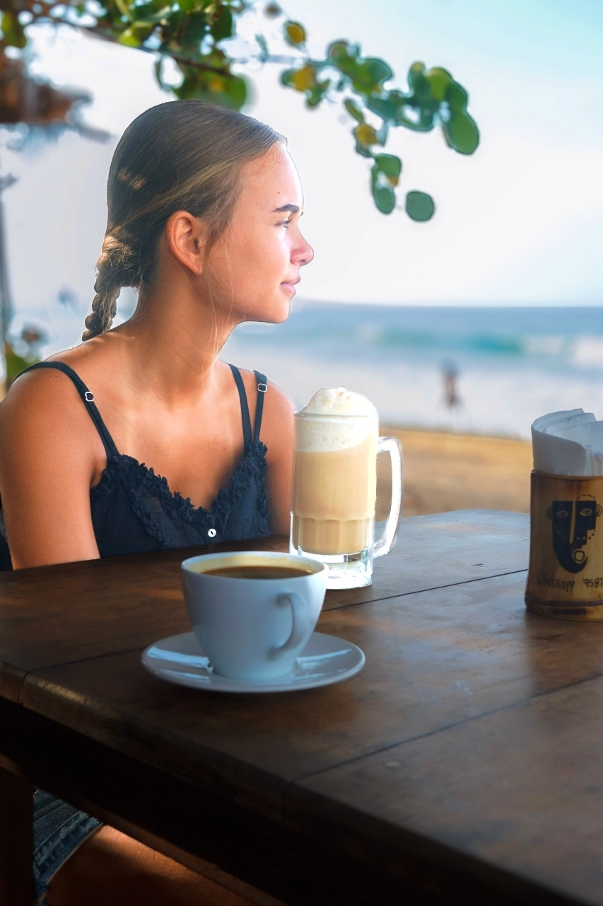 Meisje drinkt koffie aan een houten tafel aan het strand bij restaurant Un Sueño, met de golven van de Stille Oceaan op de achtergrond