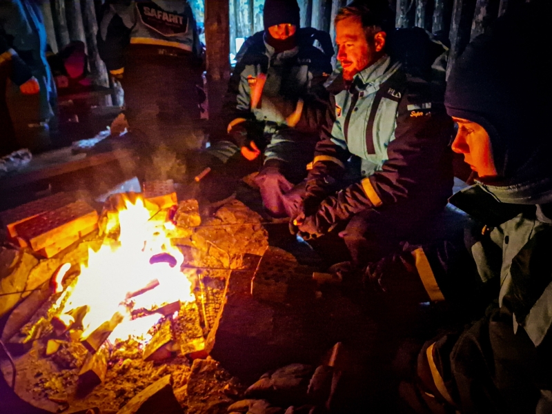 Groep zit rond het vuur in een cabin tijdens de sneeuwscooter safari in Tahko en warmt handen op