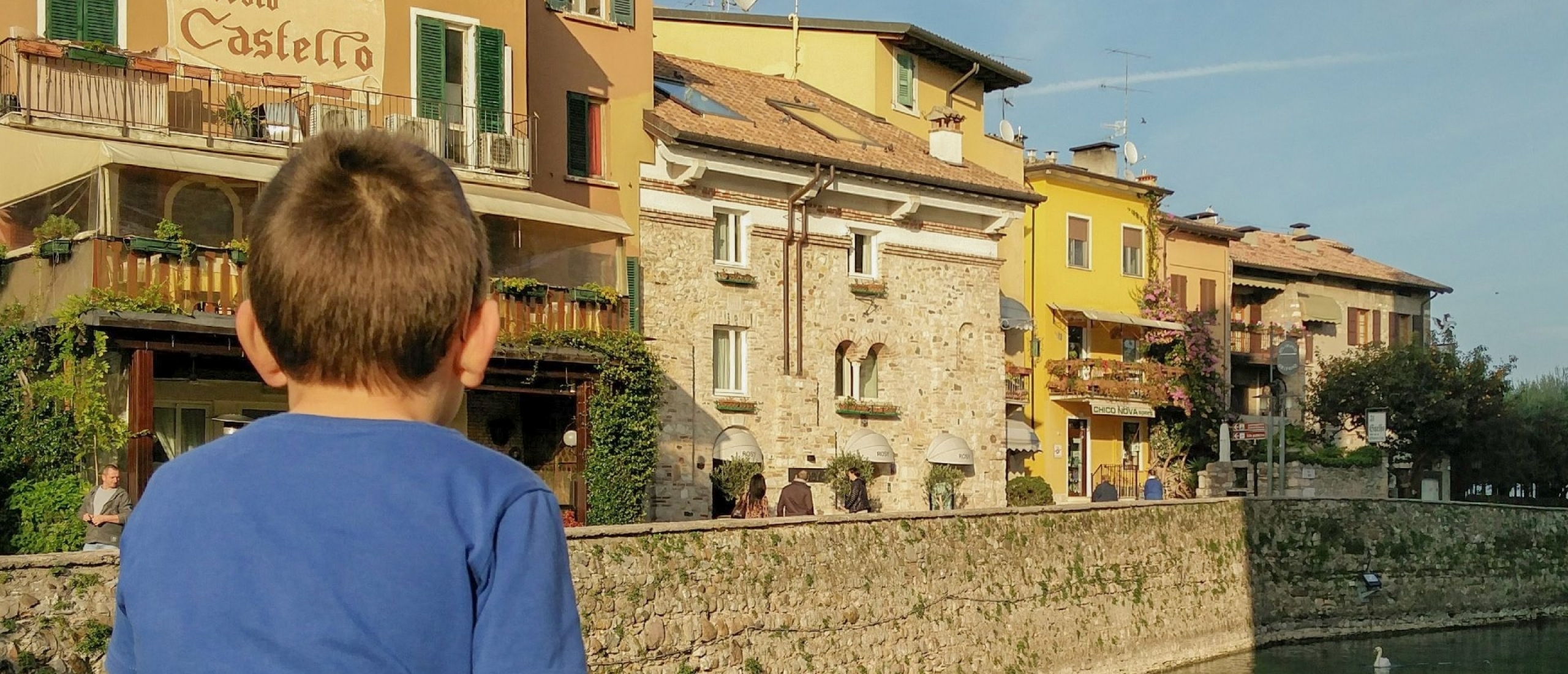 Kind zit aan de waterkant in Sirmione met uitzicht op kleurrijke huizen