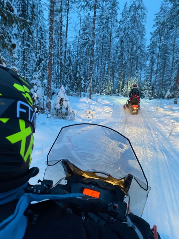POV op een sneeuwscooter door een besneeuwd bos in Tahko, met de gids die voorop rijdt
