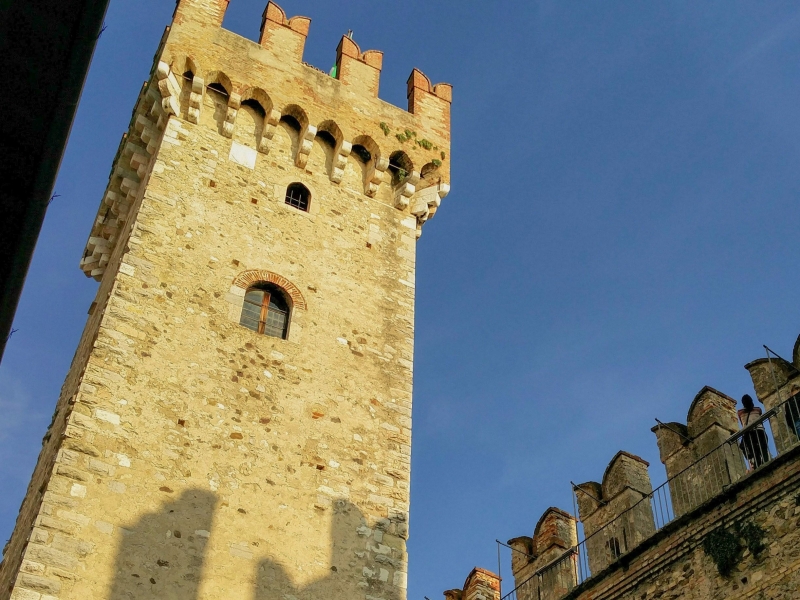 Toren en kantelen van Castello Scaligero in Sirmione tegen een blauwe lucht