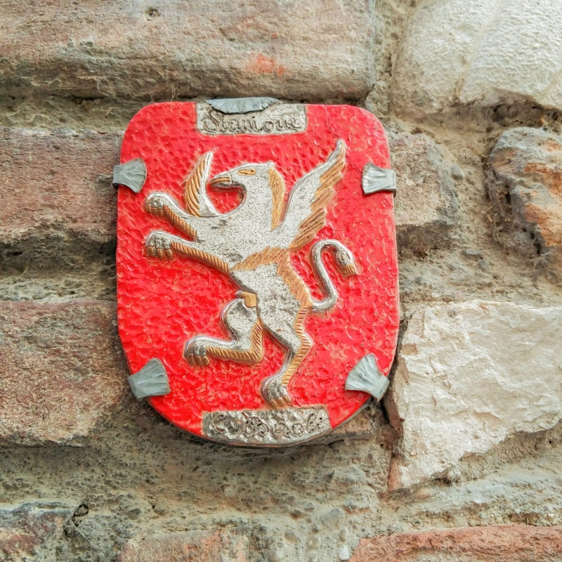 Rood keramiek wapenschild met griffioen en tekst “Sirmione Castello” op een stenen muur