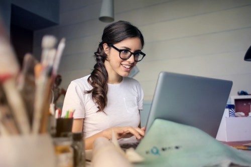 Vrouw werkt achter laptop met op haar bureau een pot kwasten