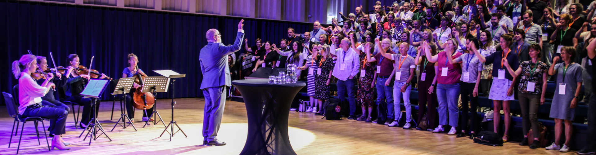 Alexander de Blaeij dirigeert een live strijkkwartet tijdens een interactieve leiderschapssessie, terwijl het publiek actief deelneemt in een volle theaterzaal.