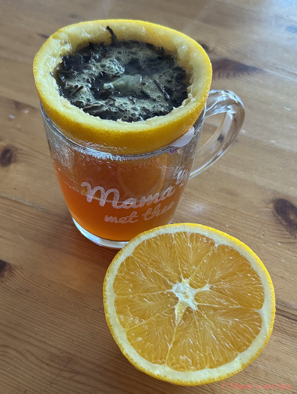 Sinaasappelthee met een sinaasappel als filter. Op de voorgrond een halve sinaasappel