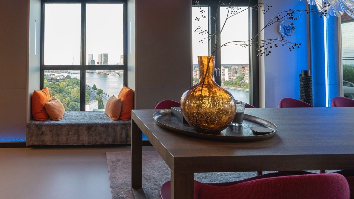 Penthouse interieur met maatwerk eettafel en raamzit, uitzicht over skyline.