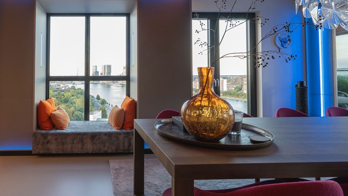 Penthouse interieur met maatwerk eettafel en raamzit, uitzicht over skyline.