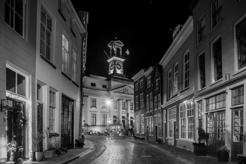 Zwart-wit nachtfoto van historisch straatje met verlichte stadhuistoren