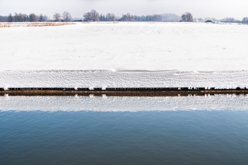 Besneeuwd weiland met blauw water op de voorgrond, als voorbeeld van contrast en eenvoud bij sneeuw fotograferen