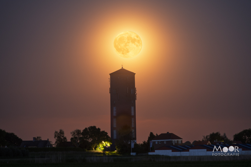 Magisch moment waarop de volle maan precies boven de watertoren rijst – een perfect getimede landschapsfoto vol sfeer.