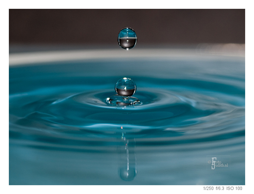 Zwevende waterdruppel boven een wateroppervlak, als voorbeeld van creatieve druppelfotografie met scherpstelling en timing