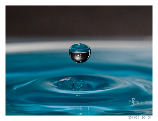 Zwevende waterdruppel boven een wateroppervlak, als voorbeeld van creatieve druppelfotografie met scherpstelling en timing