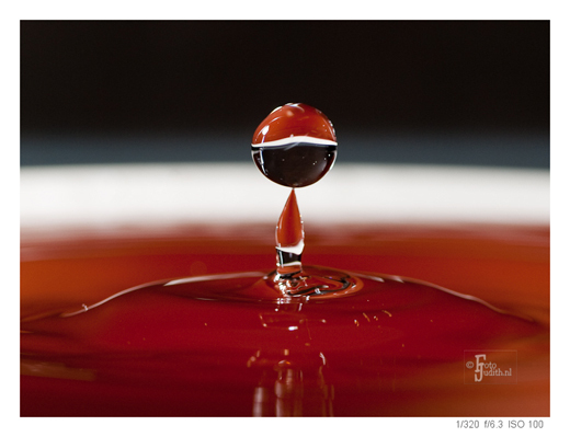Zwevende waterdruppel boven een wateroppervlak, als voorbeeld van creatieve druppelfotografie met scherpstelling en timing