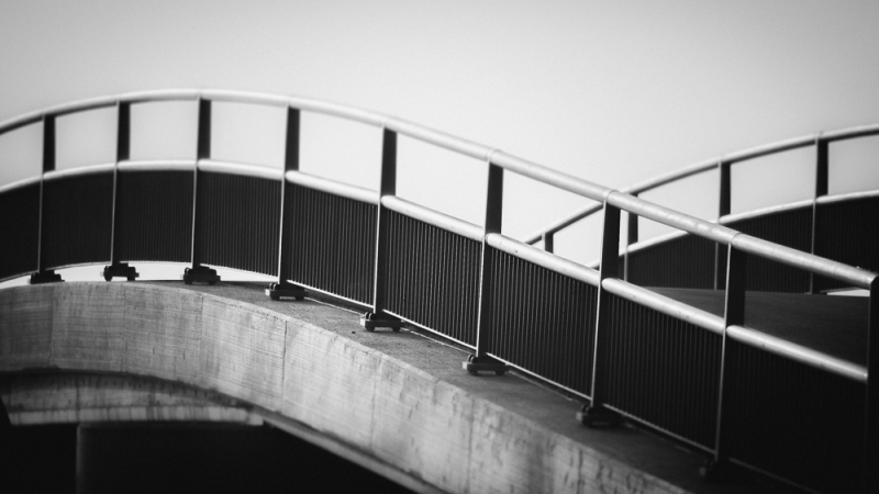 Minimalistische zwart-witfoto van een brug met metalen reling en gebogen vormen