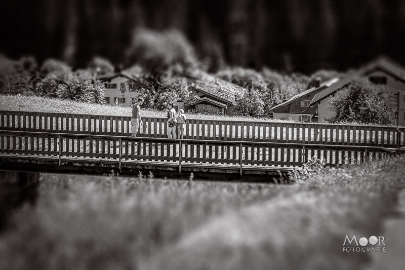 Tilt-shift foto met miniatuureffect  **Alternatieve tekst:** Zwart-wit foto met tilt-shift effect waardoor een hek en huisjes lijken op een kleine miniatuurwereld.