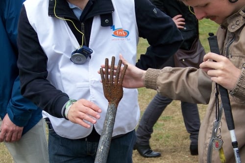 Een jongen met een witte stok tast een metalen beeld af in de openlucht. De uitgestrekte vingers van het beeld raken de zijne.