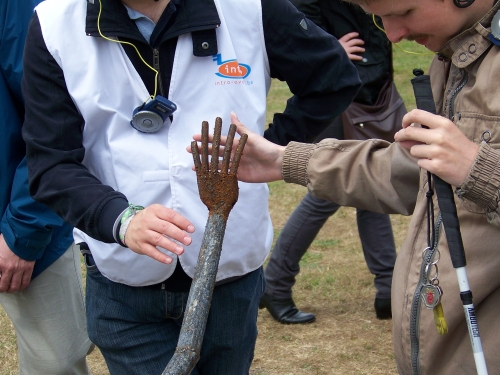 Een jongen met een witte stok tast een metalen beeld af in de openlucht. De uitgestrekte vingers van het beeld raken de zijne.