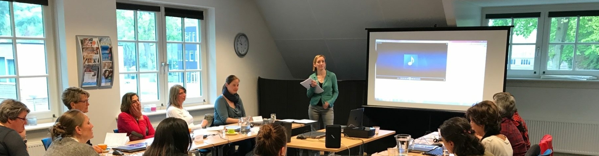 Een tiental mensen volgt een workshop bij Susanne, die voor de groep staat.