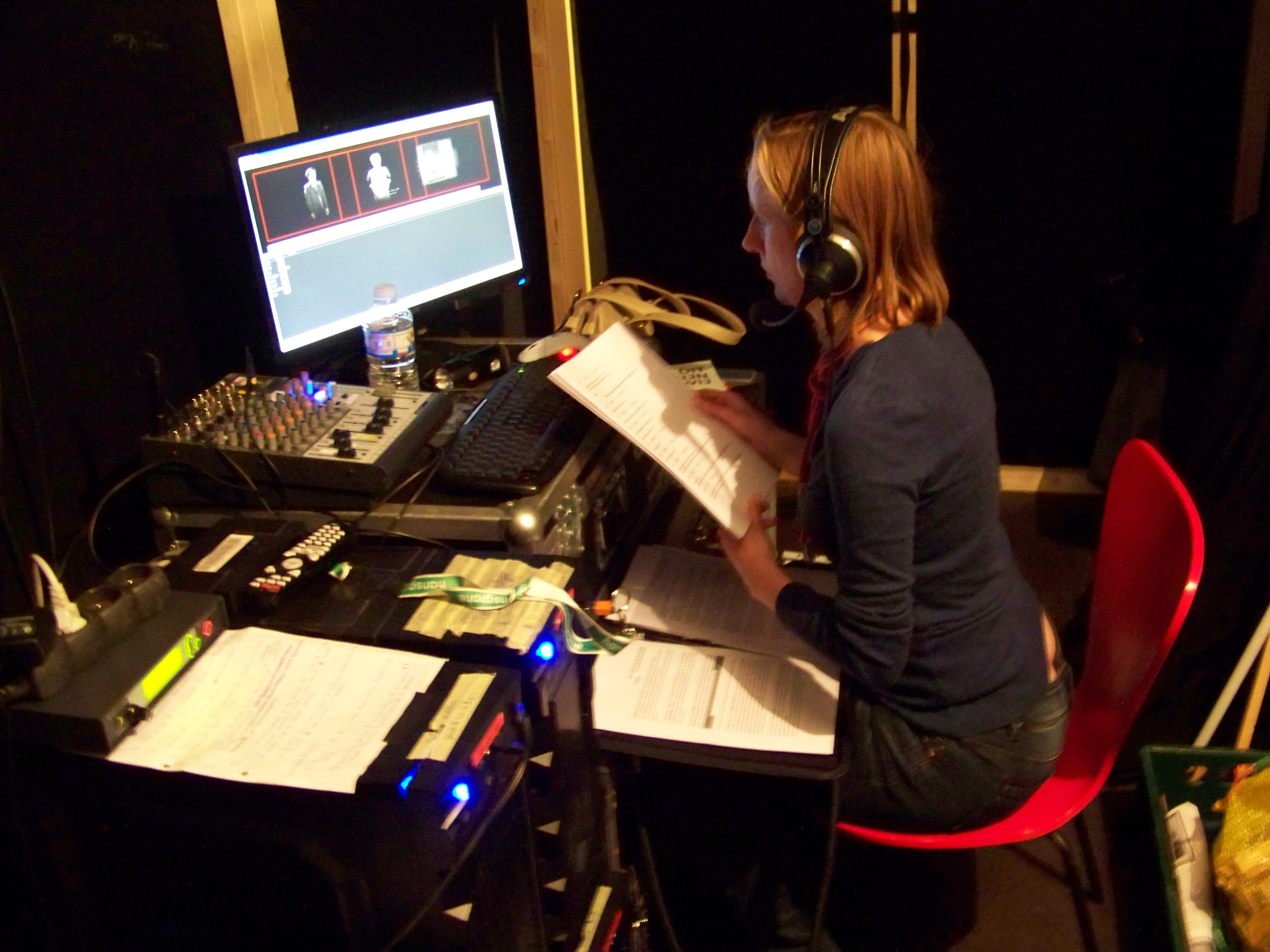 Susanne zit aan een tafel in de projectieruimte. Een klein lampje verlicht haar script.