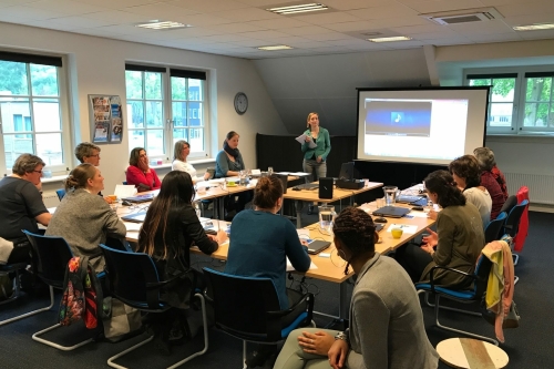 Een tiental mensen volgt een workshop bij Susanne, die voor de groep staat.