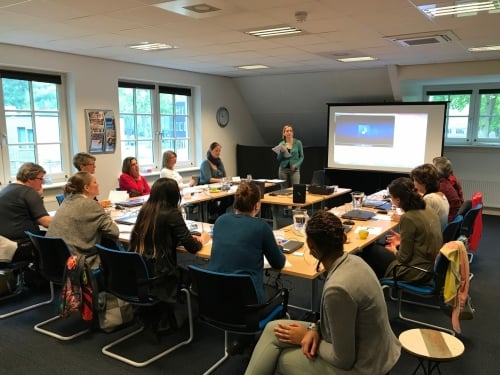 Een tiental mensen volgt een workshop bij Susanne, die voor de groep staat.