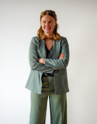 Nienke Vink staat met gekruiste armen en een vriendelijke glimlach in een groene outfit. Een professioneel portret dat haar betrokkenheid en expertise in dierlijke voeding weerspiegelt.