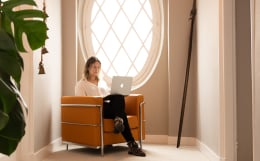 vrouw op oranje stoel werkt op laptop