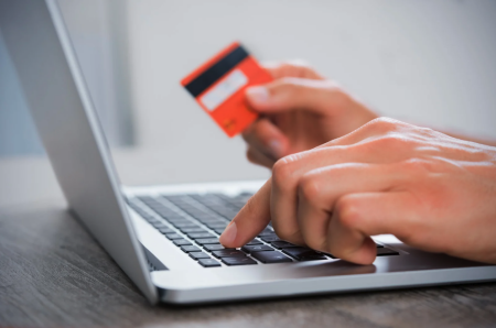 iemand die achter een laptop zit met een betaalkaart in de hand
